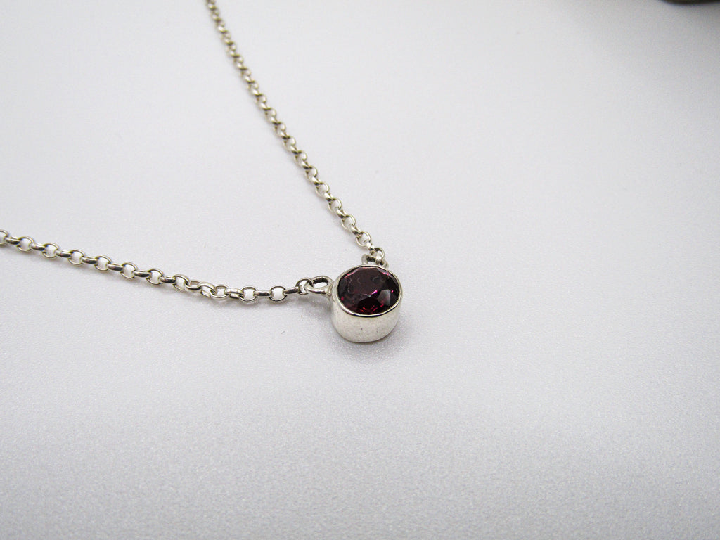 Silver necklace with a dark gemstone pendant on a light gray background
