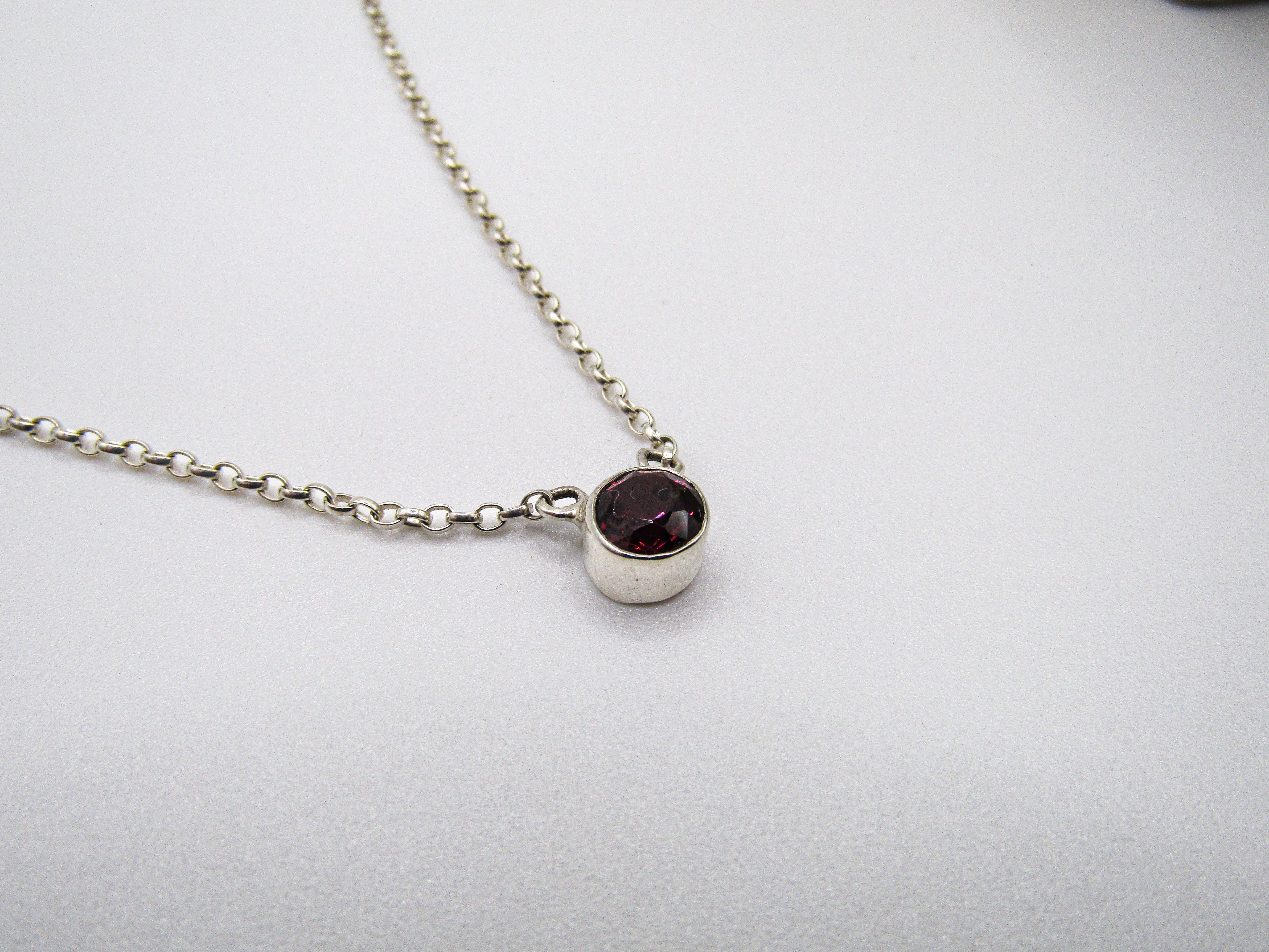 Silver necklace with a dark gemstone pendant on a light gray background
