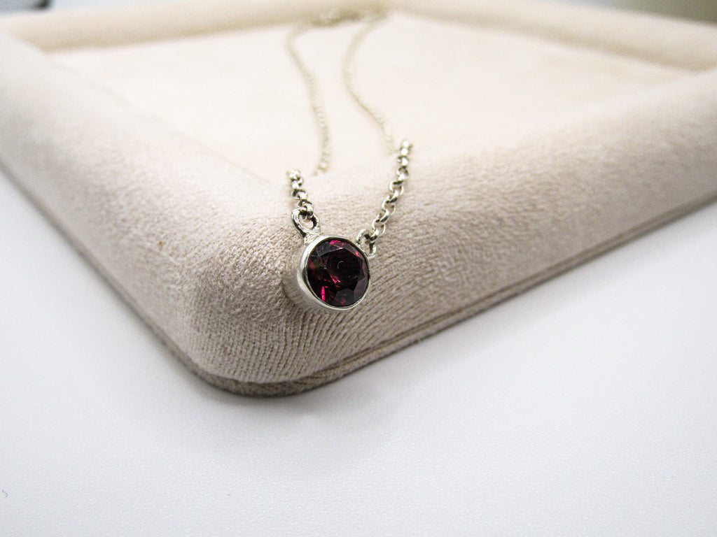 Necklace with a red gemstone pendant on a beige cushion