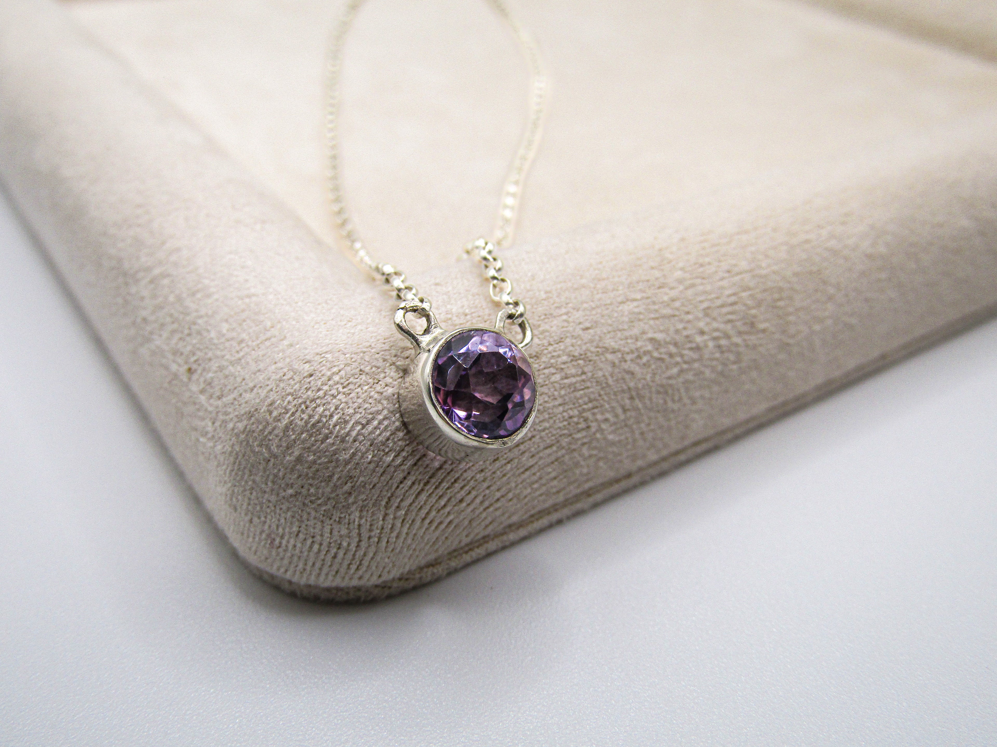 Necklace with a purple gemstone pendant on a beige cushion