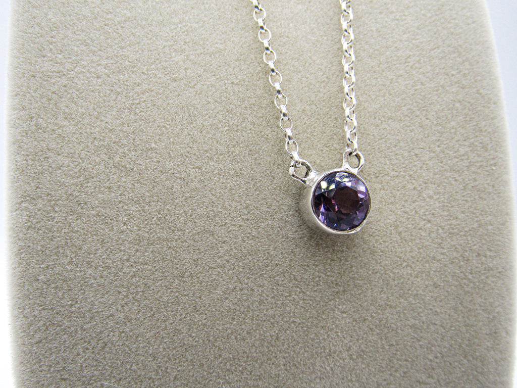 Silver necklace with a purple gemstone on a gray background
