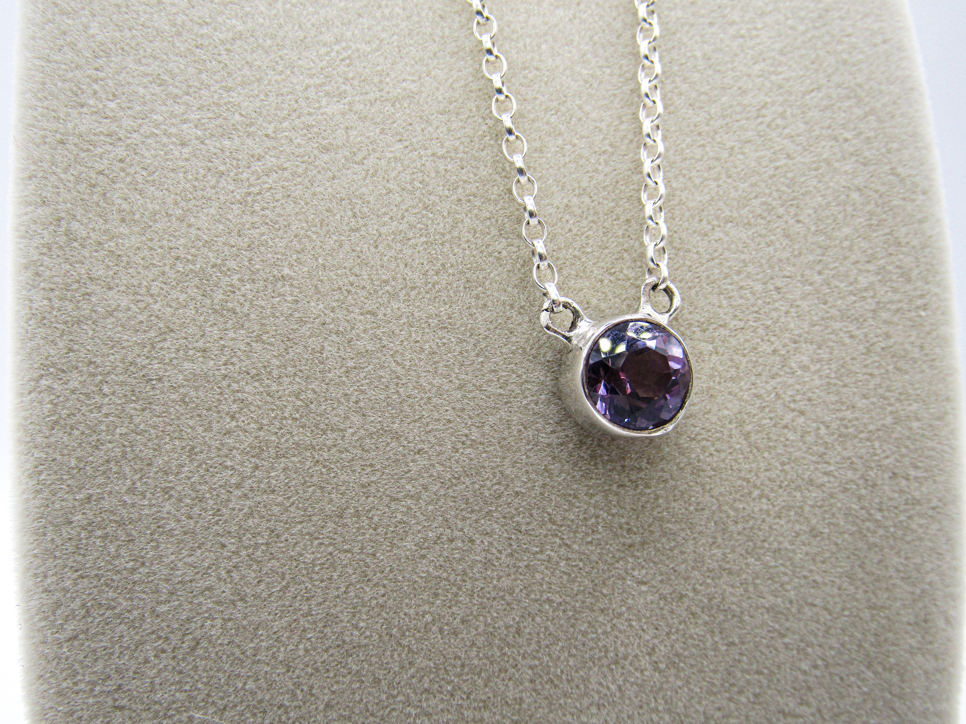 Silver necklace with a purple gemstone on a gray background