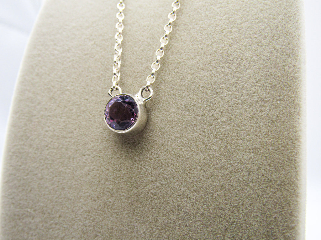 Silver necklace with a purple gemstone pendant on a gray surface