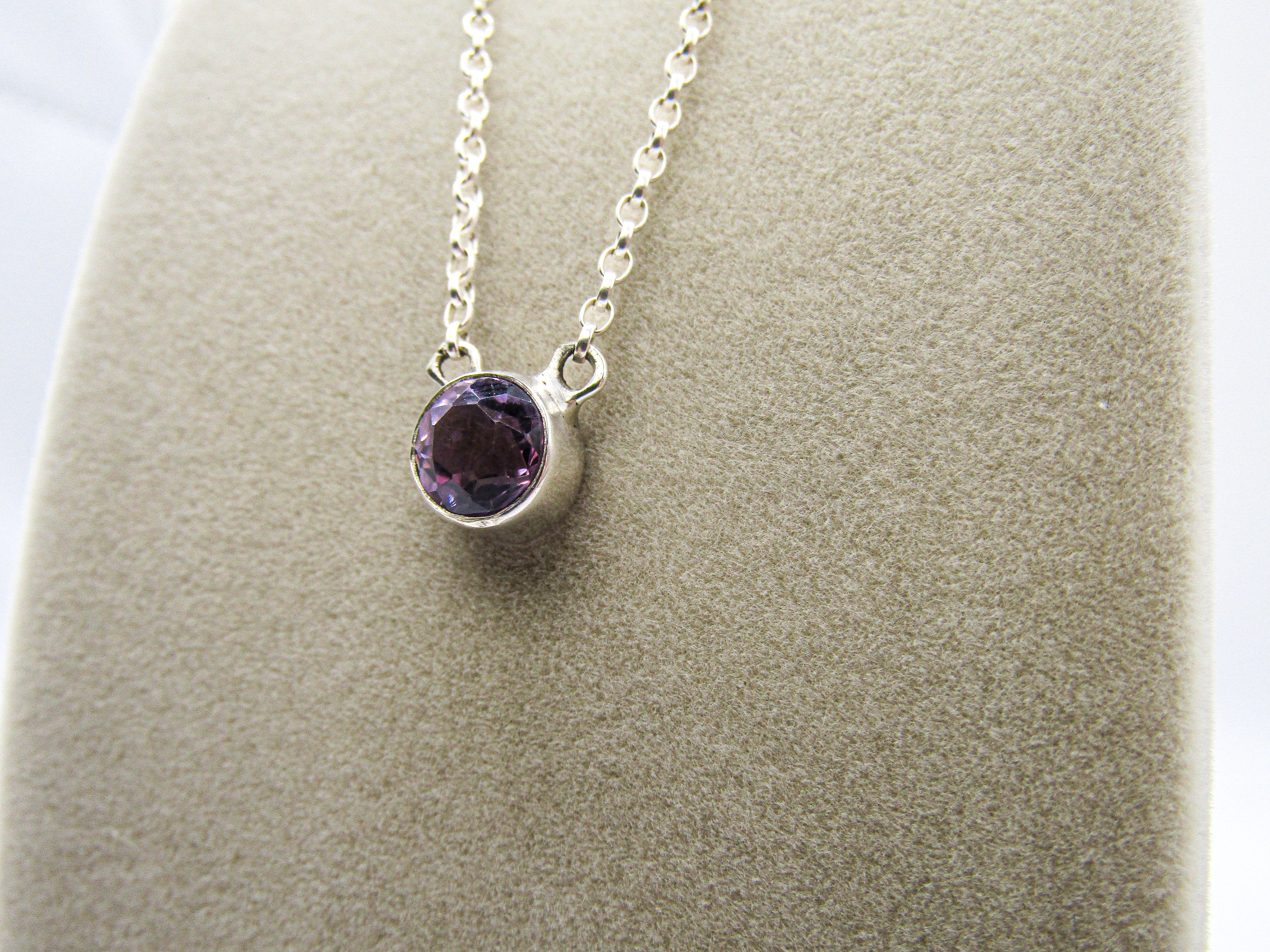Silver necklace with a purple gemstone pendant on a gray surface