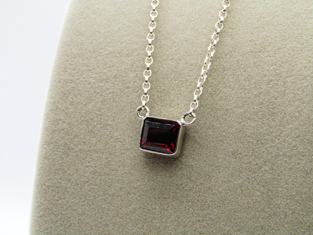 Silver necklace with a square red gemstone pendant on a gray surface.