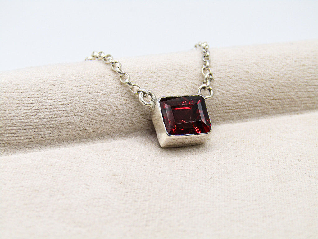 Silver necklace with a red gemstone pendant on a white fabric background