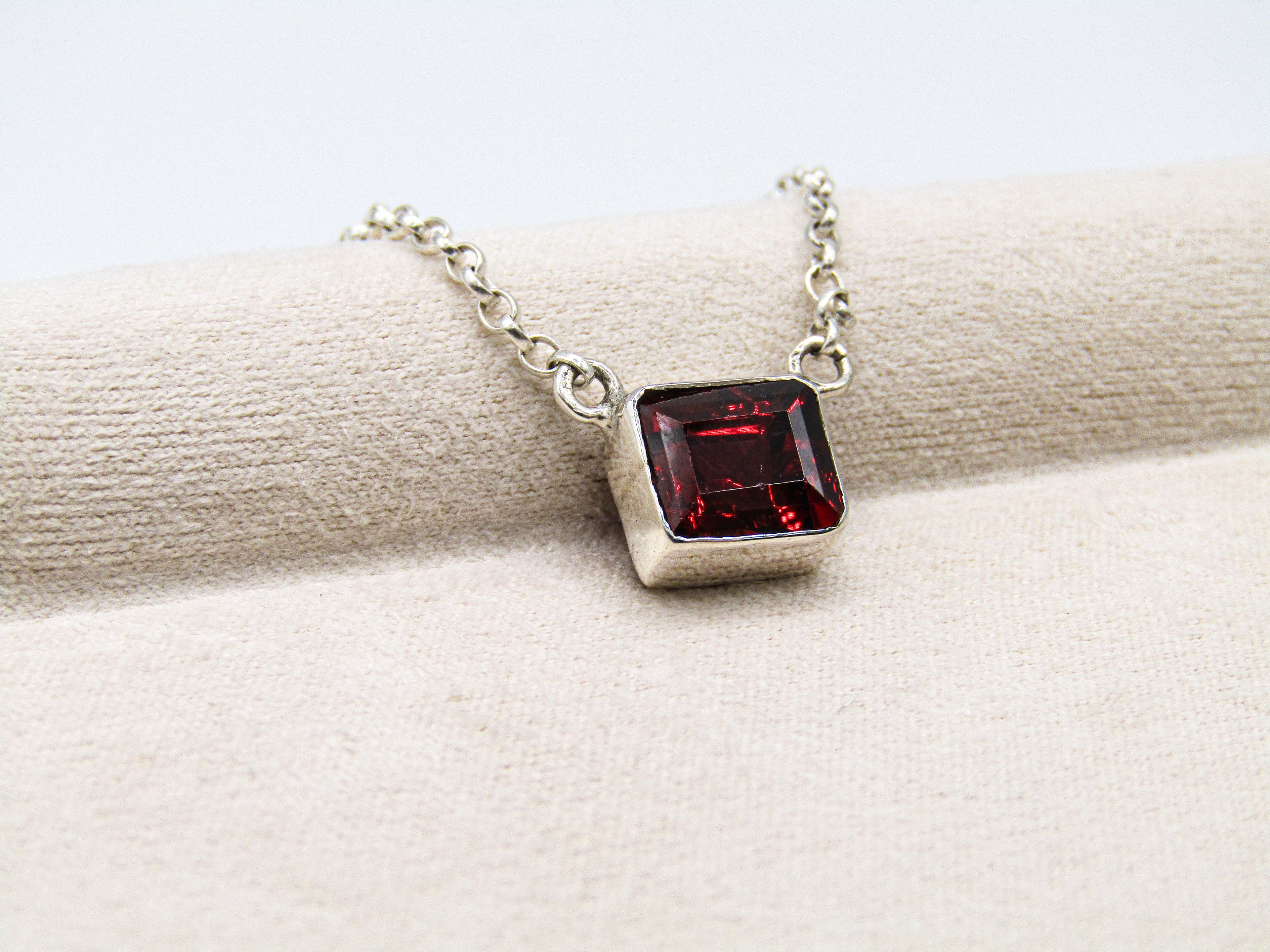 Silver necklace with a red gemstone pendant on a white fabric background