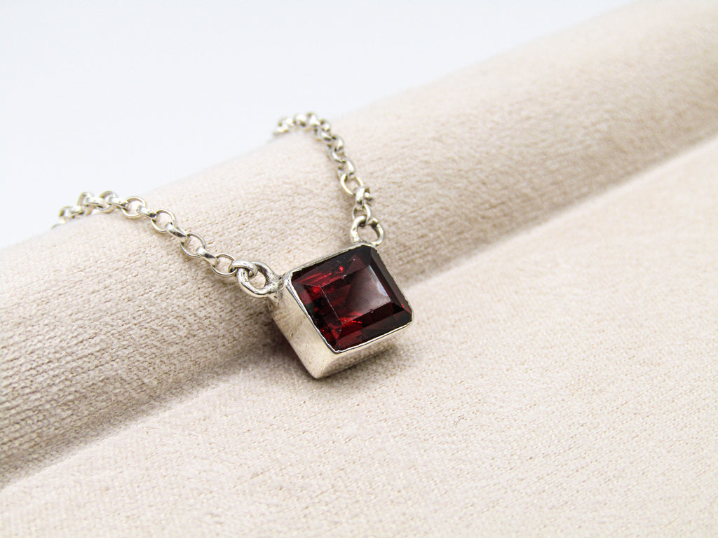 Silver necklace with a red gemstone pendant on a beige surface