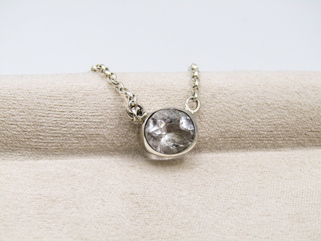 Silver necklace with a clear gemstone pendant on a beige fabric background