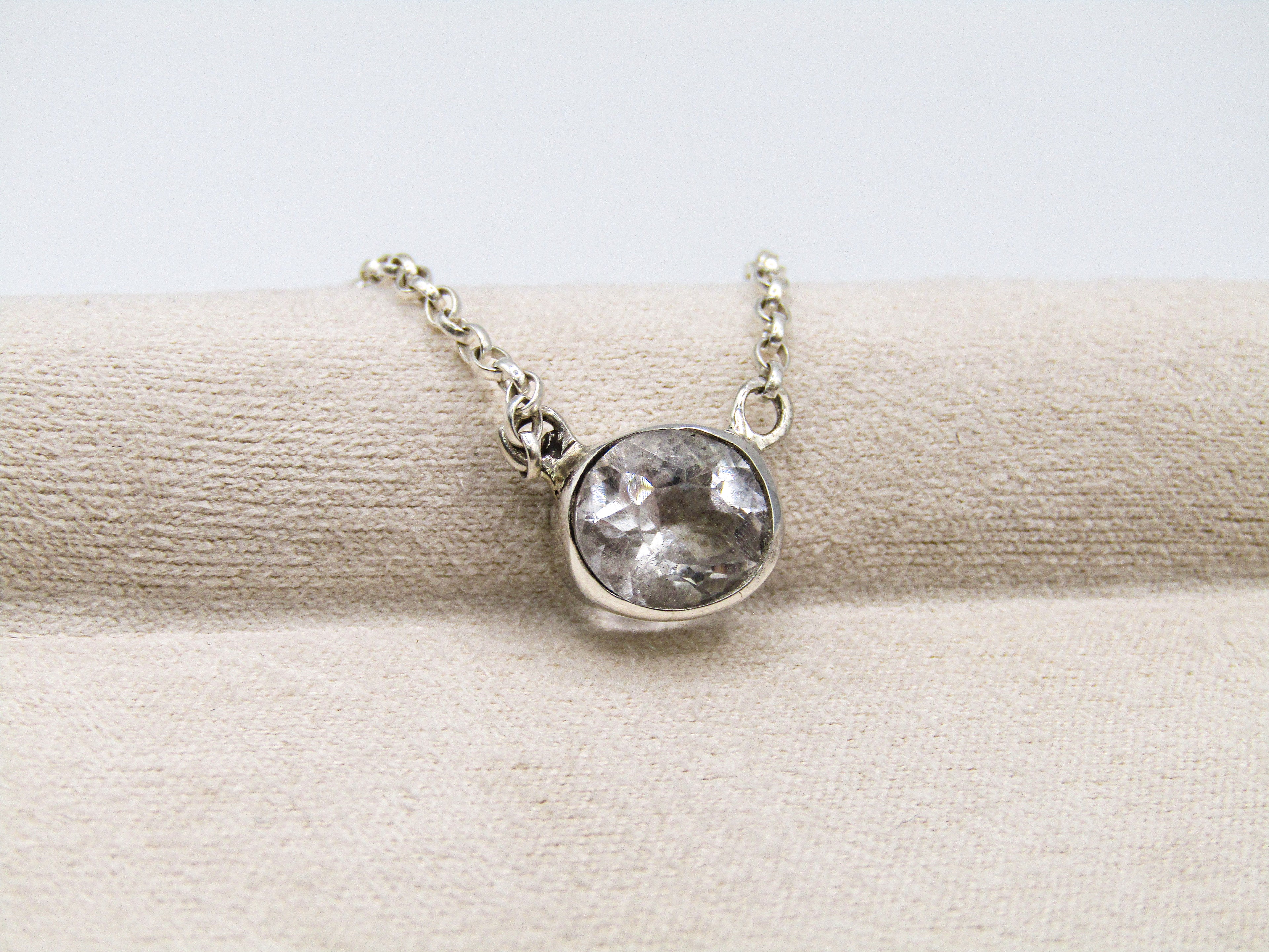 Silver necklace with a clear gemstone pendant on a beige fabric background