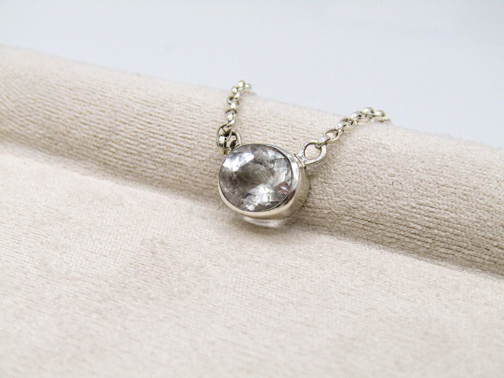 Silver necklace with a clear gemstone on a beige fabric background