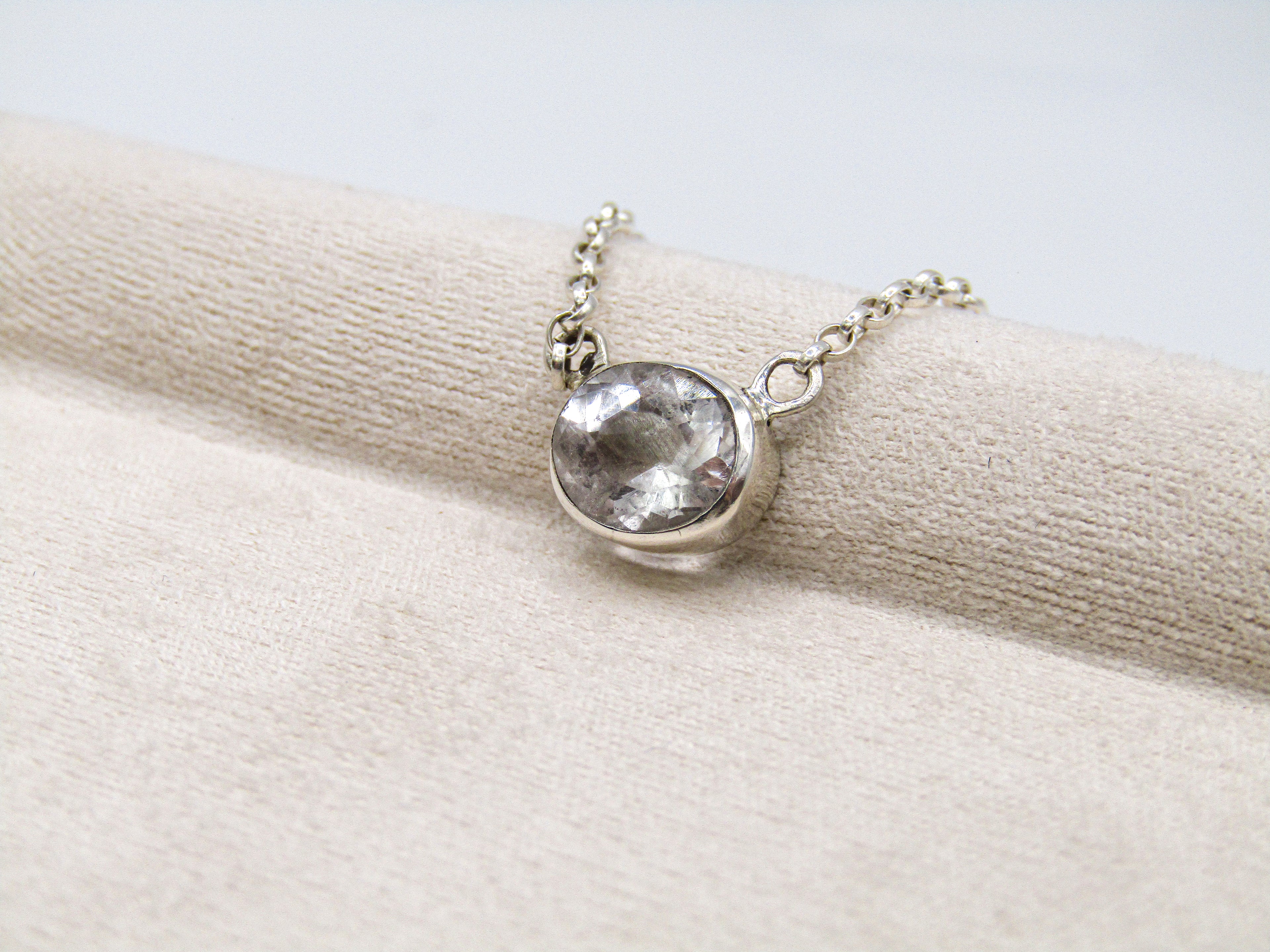 Silver necklace with a clear gemstone on a beige fabric background