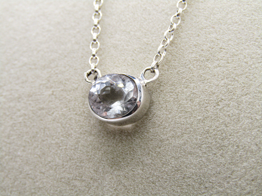 Silver necklace with a clear gemstone on a beige background
