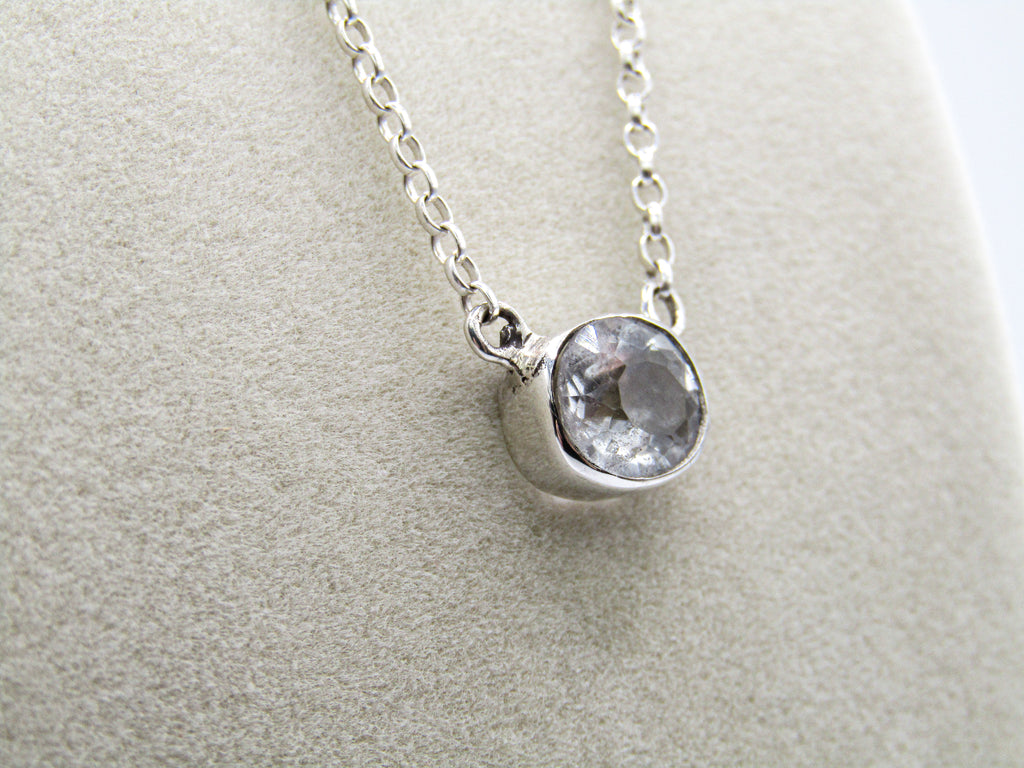 Silver necklace with a round gemstone pendant on a light gray background