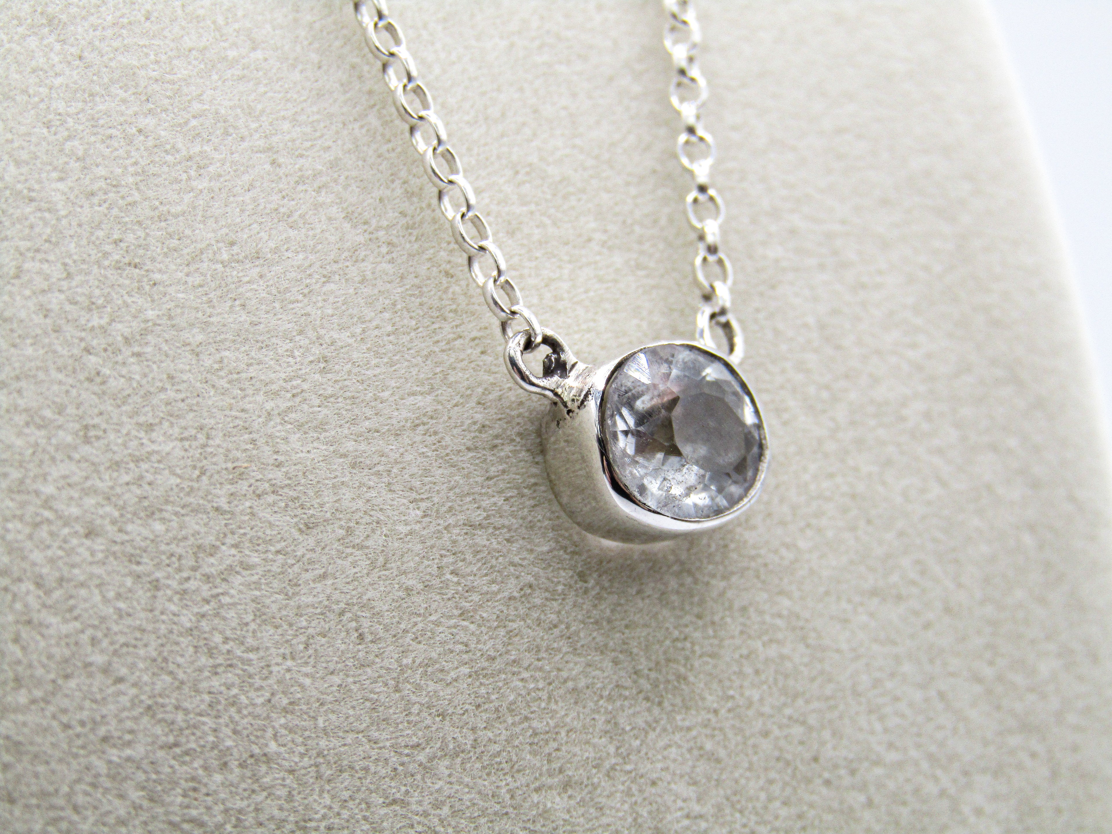 Silver necklace with a round gemstone pendant on a light gray background