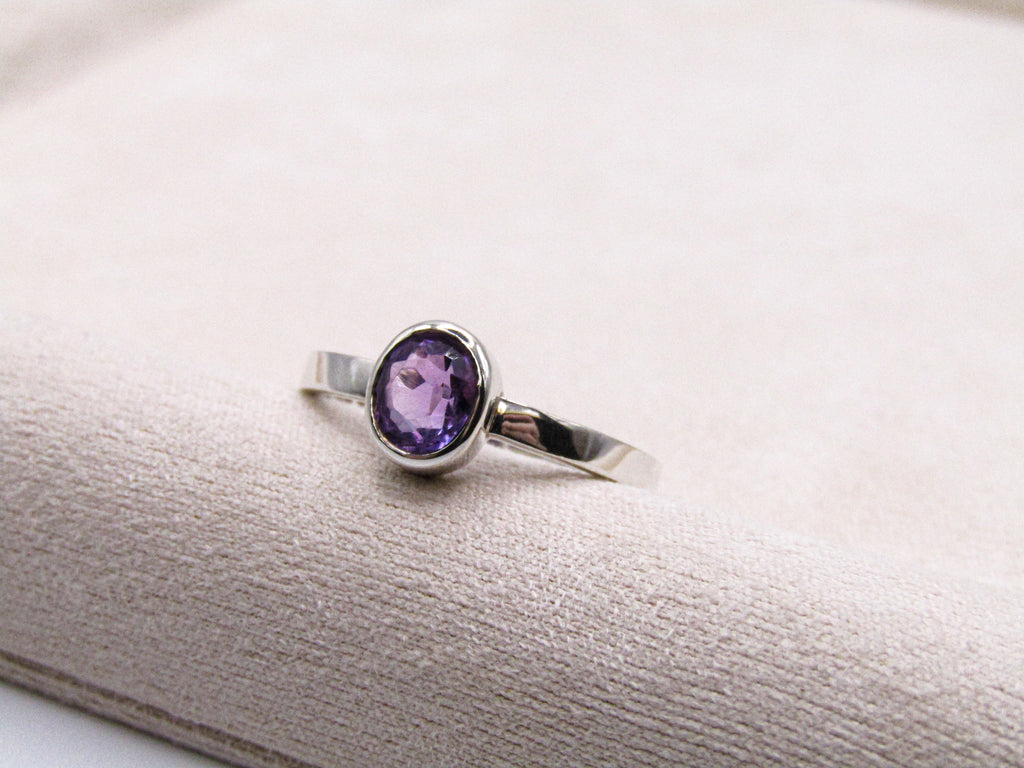 Silver ring with a purple gemstone on a textured white surface