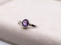 Silver ring with a purple gemstone on a textured white surface