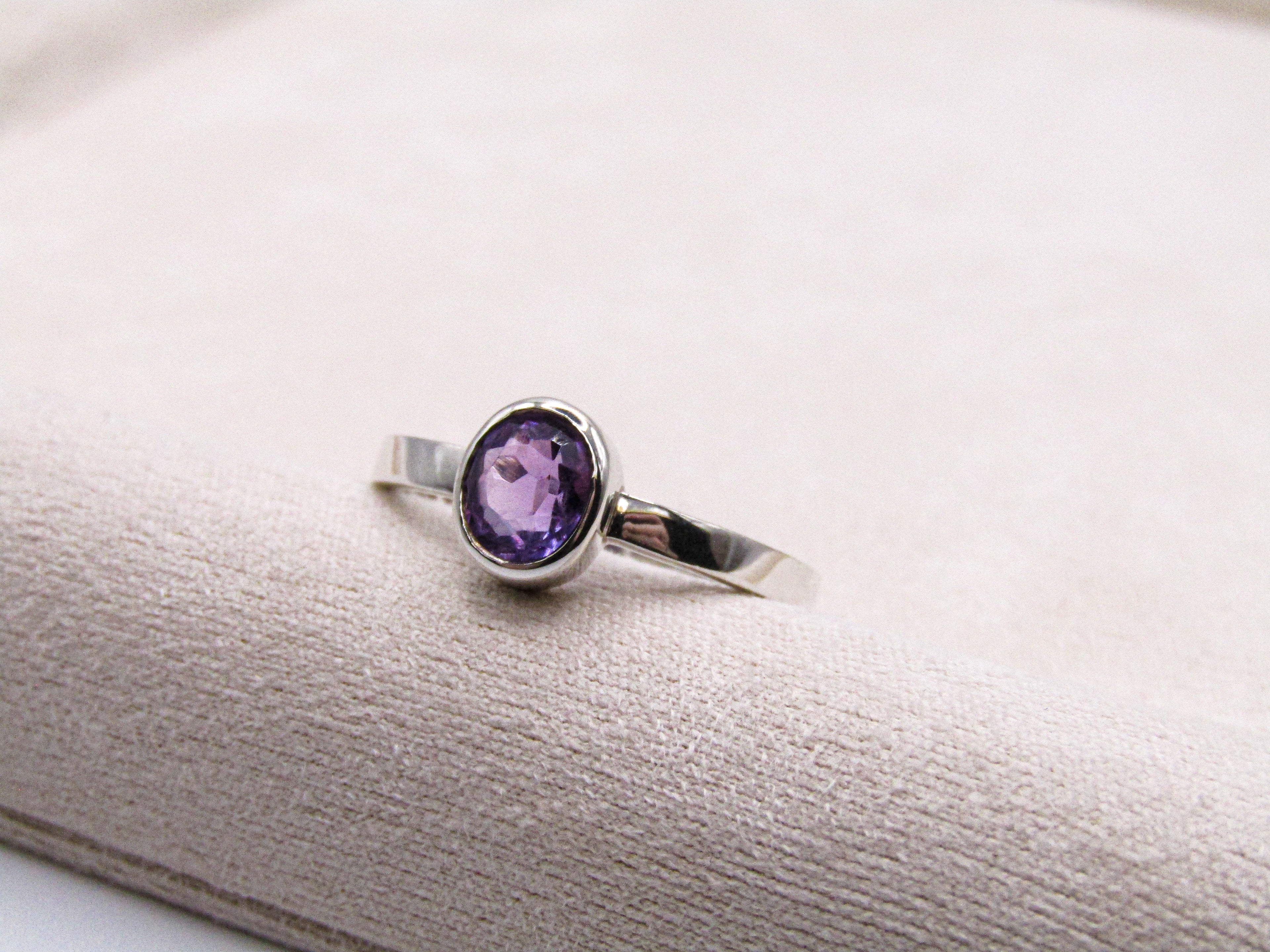 Silver ring with a purple gemstone on a textured white surface