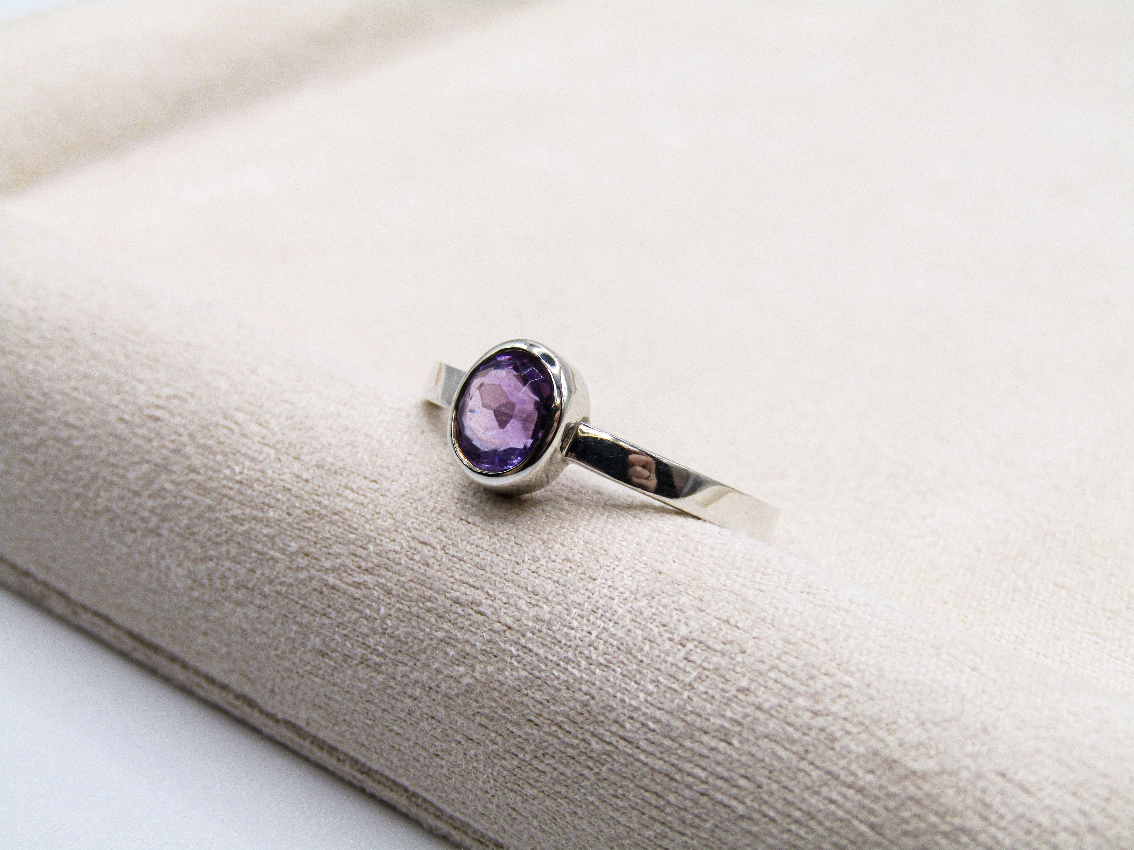 Silver ring with a purple gemstone on a white surface