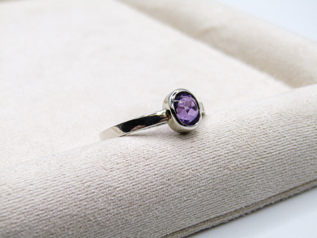 Silver ring with a purple gemstone on a textured white surface