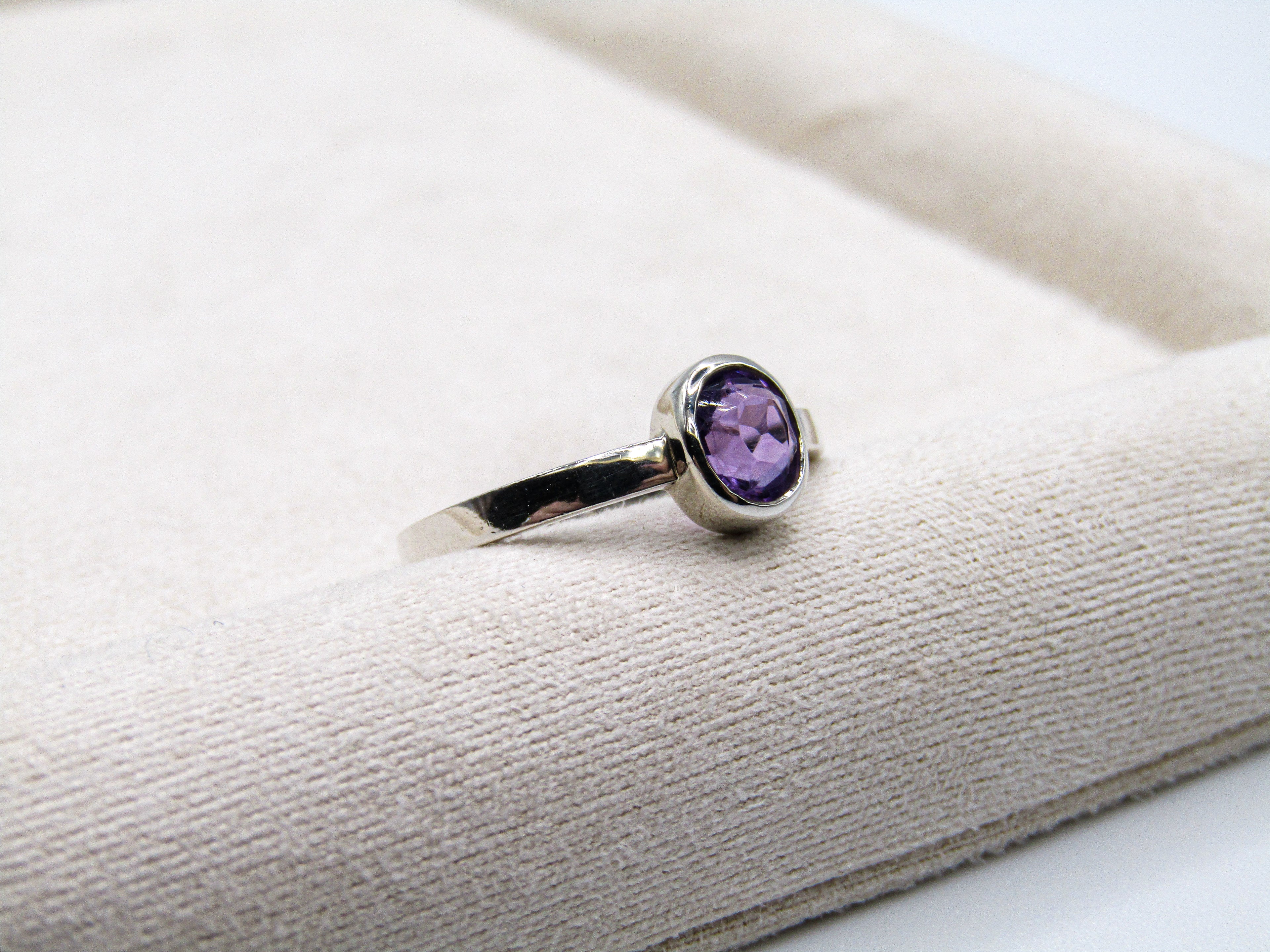 Silver ring with a purple gemstone on a textured white surface