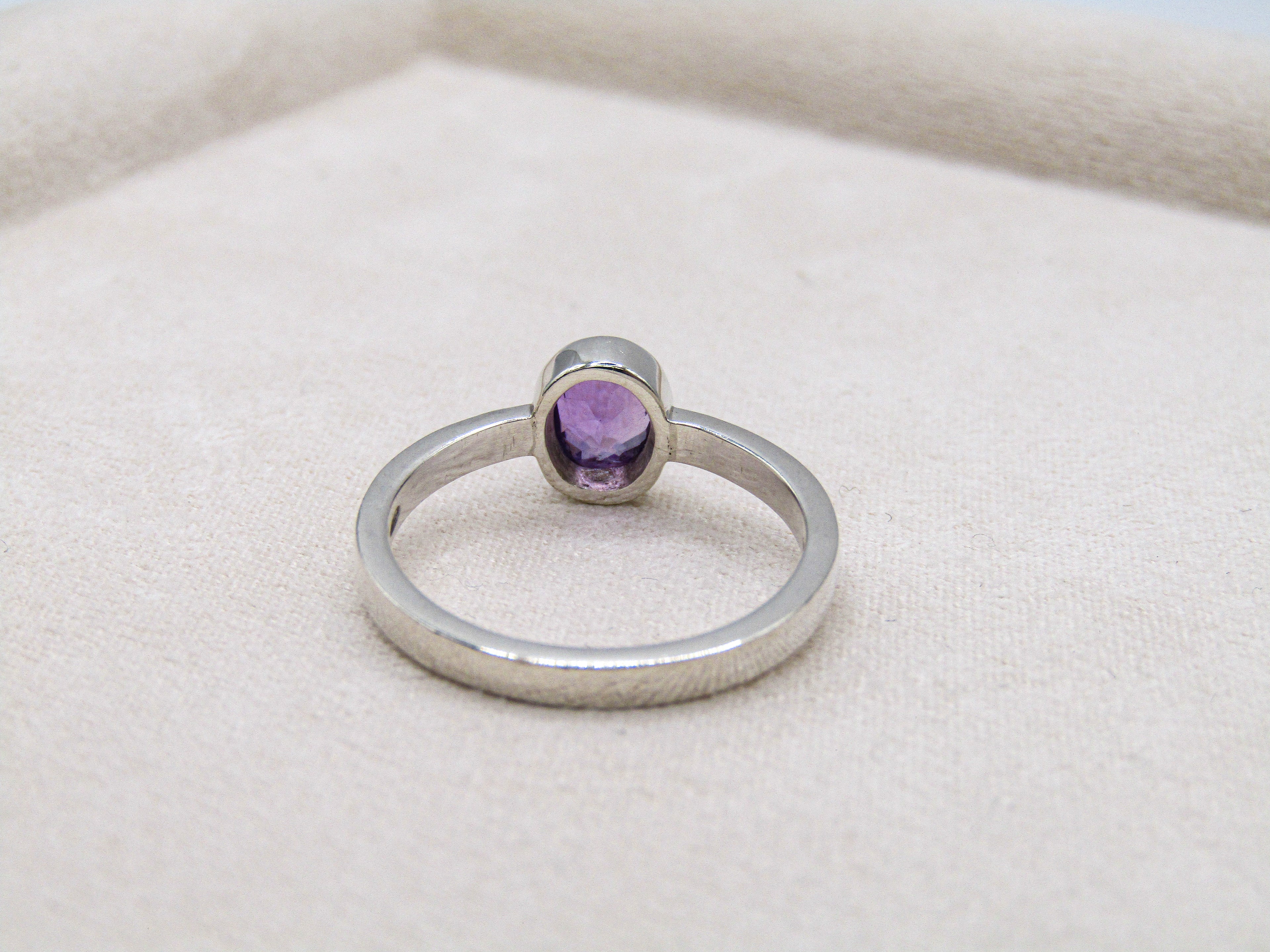 Silver ring with a purple gemstone on a beige fabric background