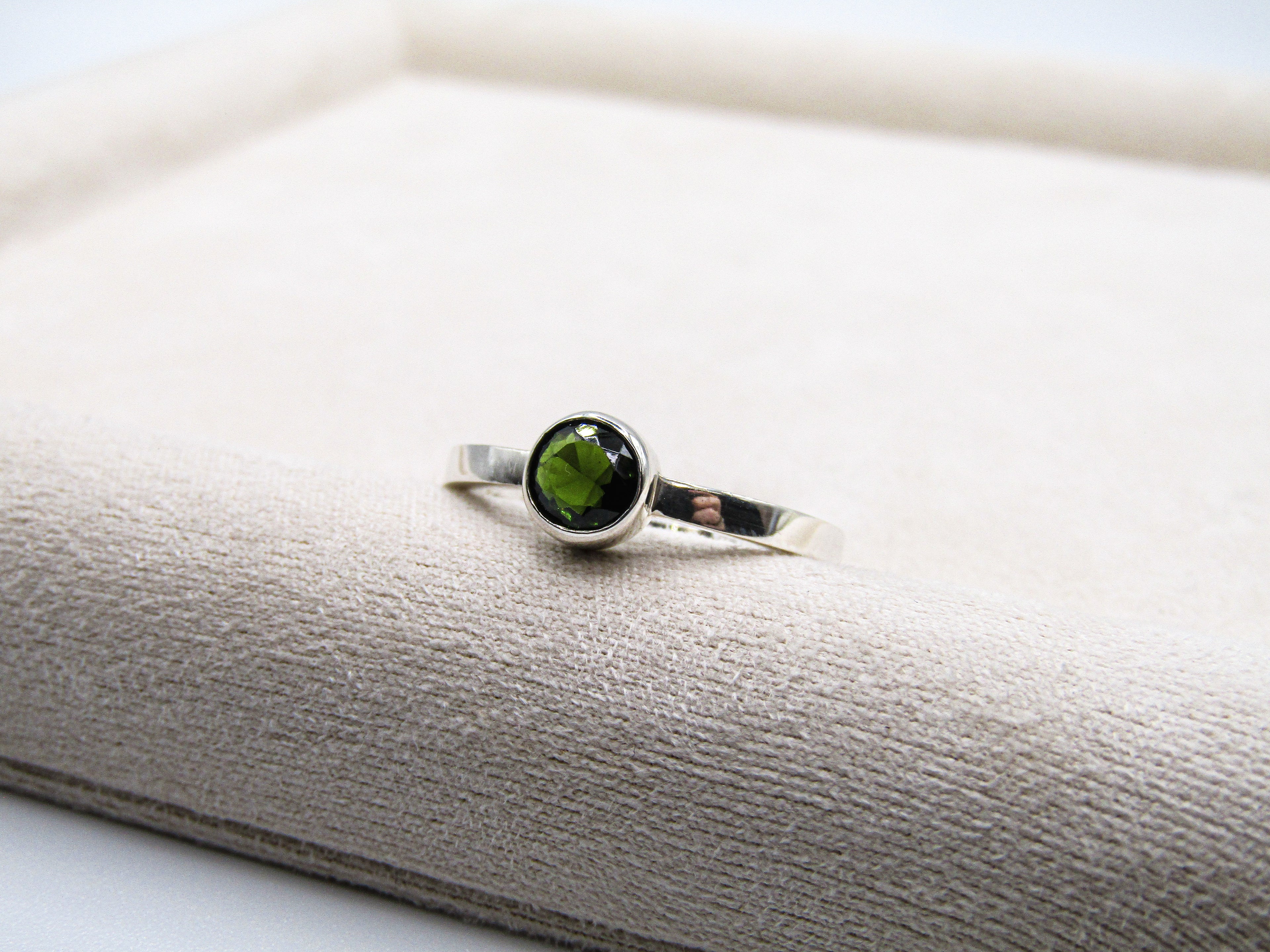 Silver ring with a green gemstone on a white surface
