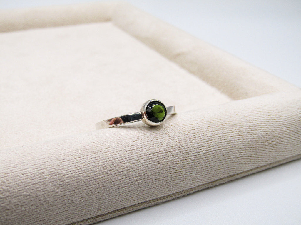 Silver ring with a green gemstone on a textured beige surface