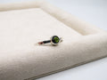 Silver ring with a green gemstone on a textured beige surface