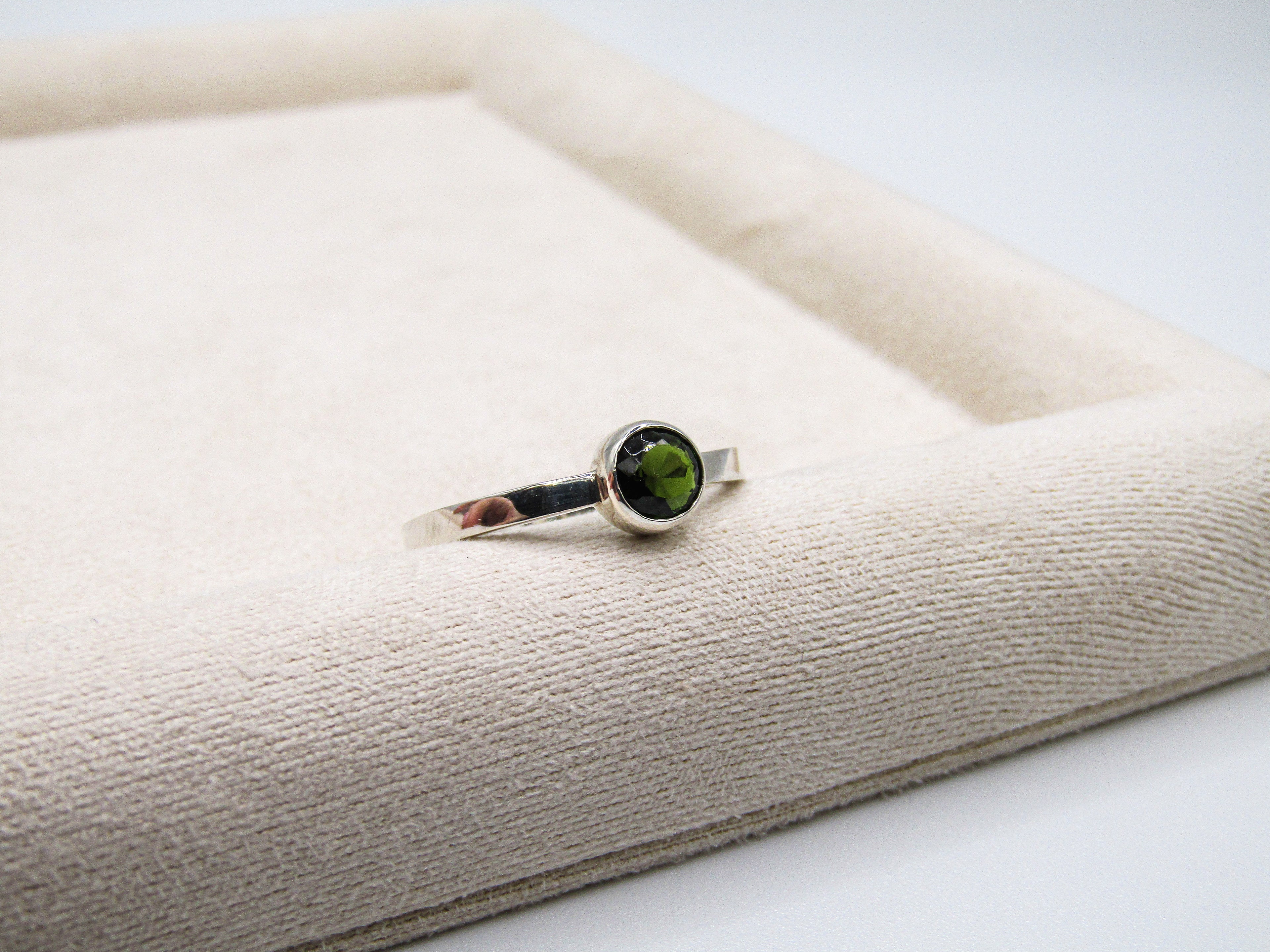 Silver ring with a green gemstone on a textured beige surface