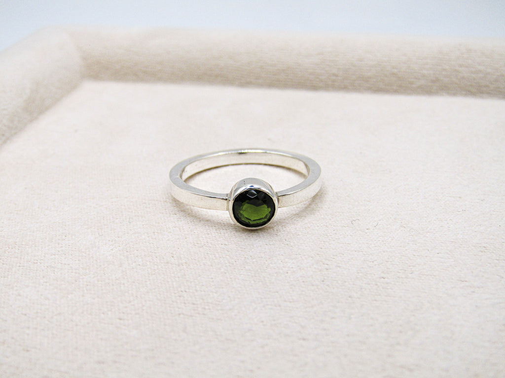 Silver ring with a green gemstone on a white fabric background