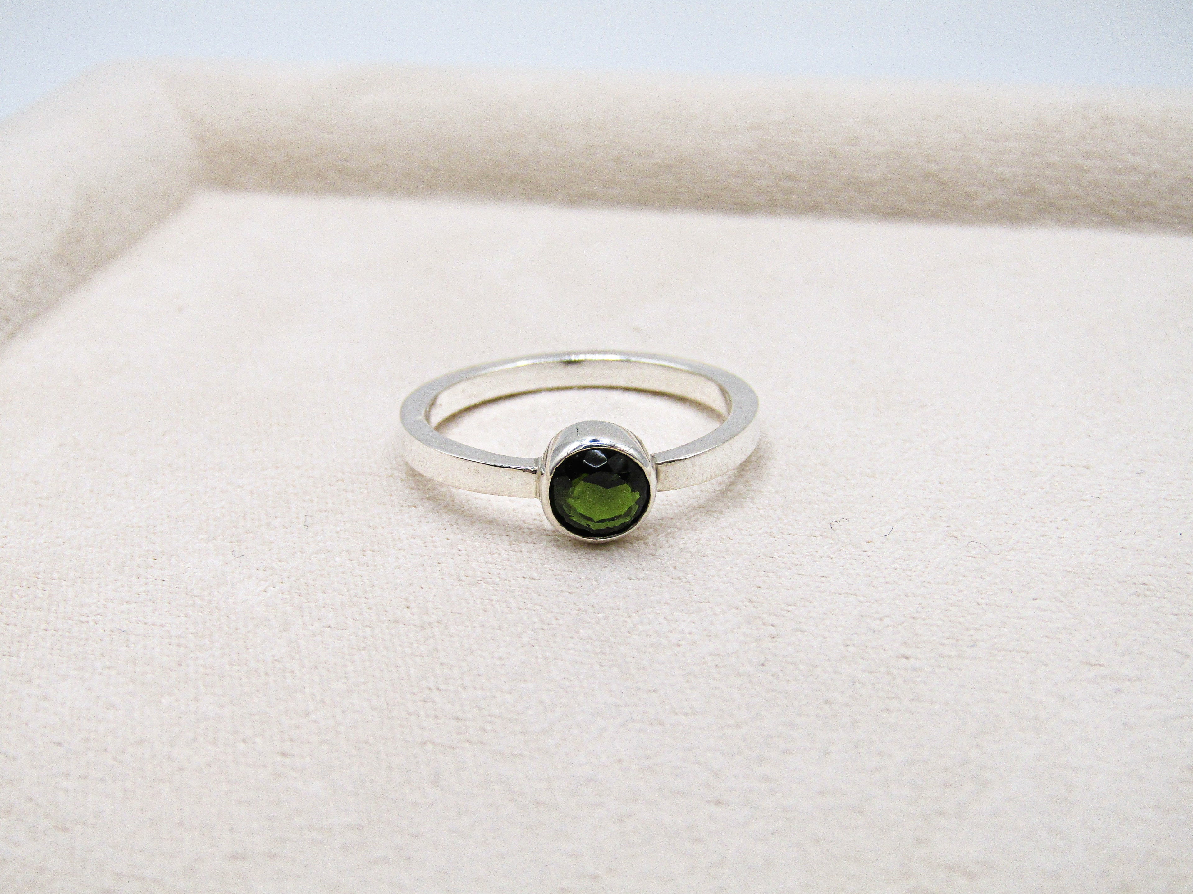 Silver ring with a green gemstone on a white fabric background