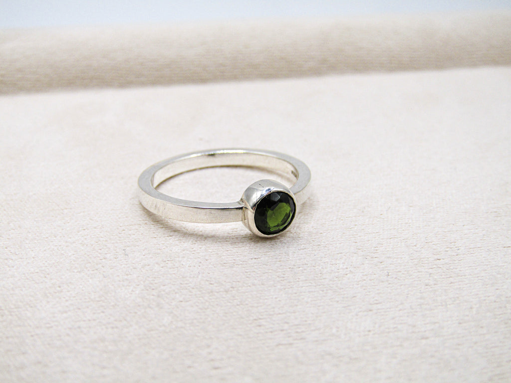 Silver ring with a green gemstone on a white fabric background