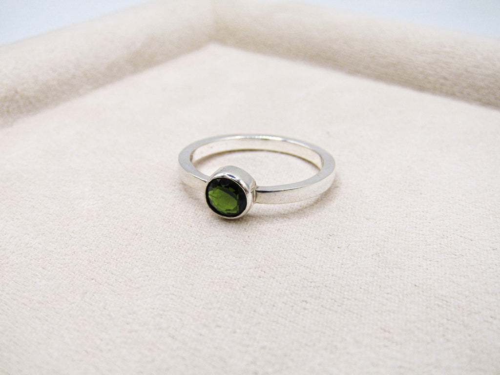 Silver ring with a green gemstone on a white fabric background