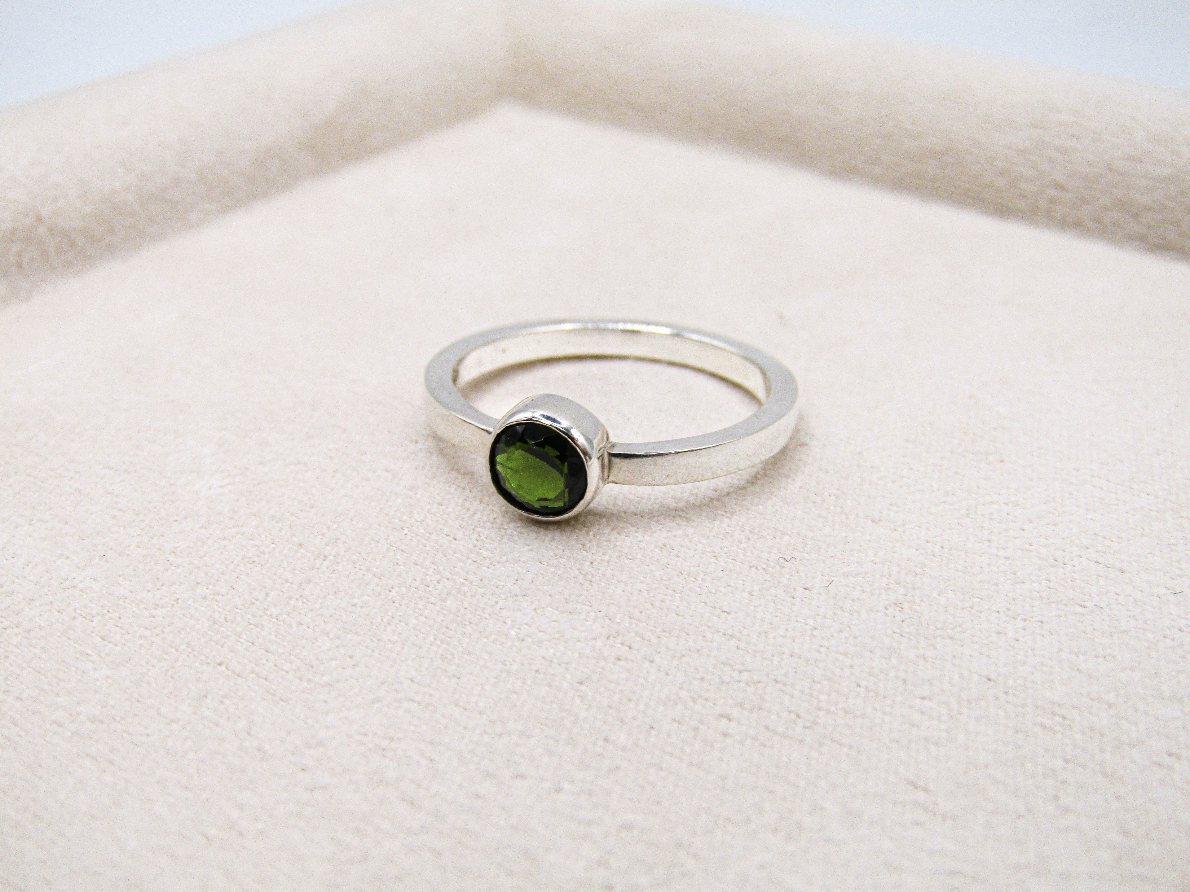 Silver ring with a green gemstone on a white fabric background