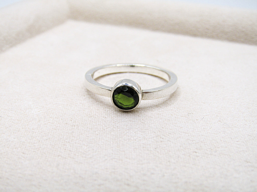 Silver ring with a green gemstone on a white fabric background