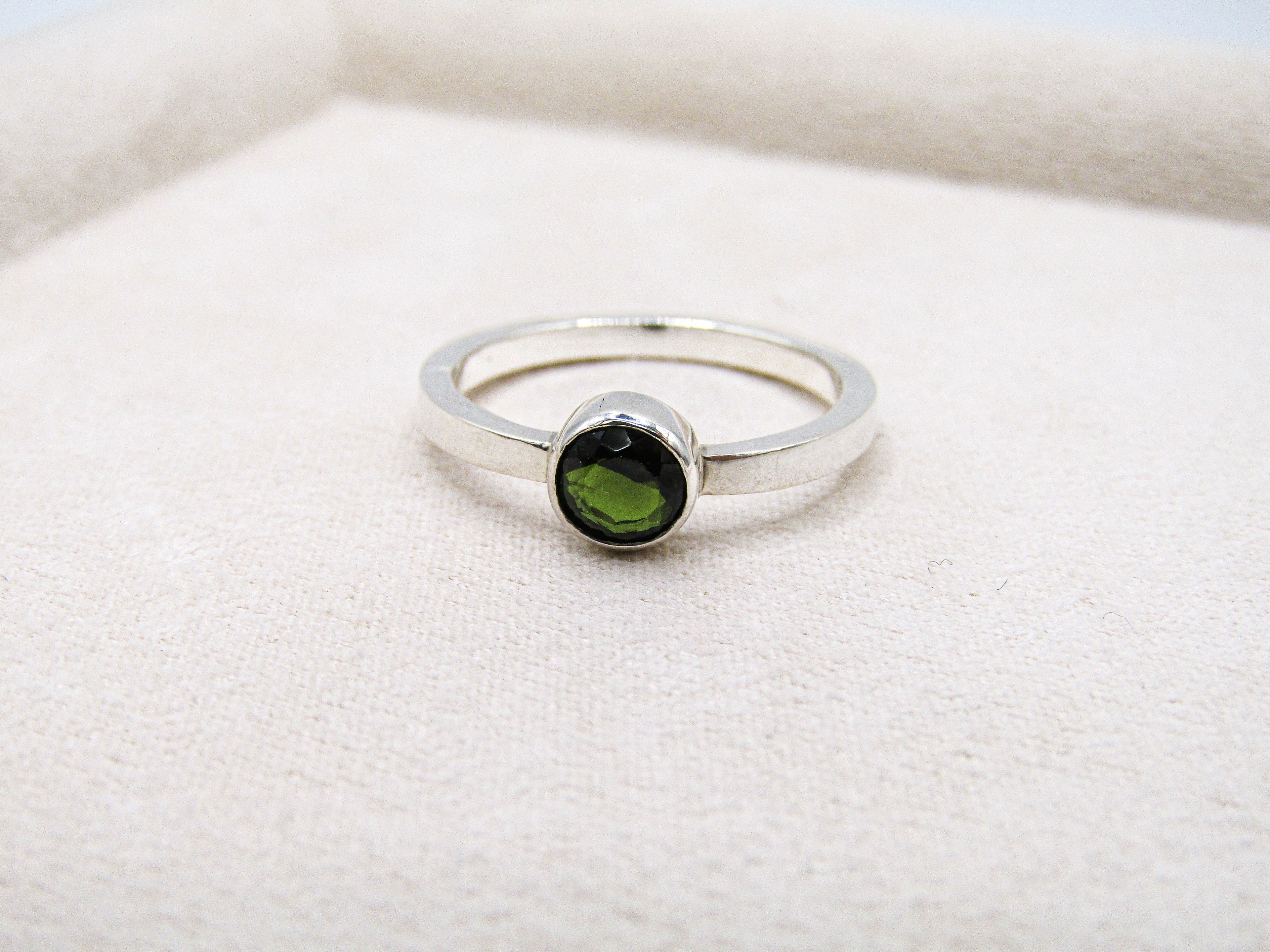 Silver ring with a green gemstone on a white fabric background