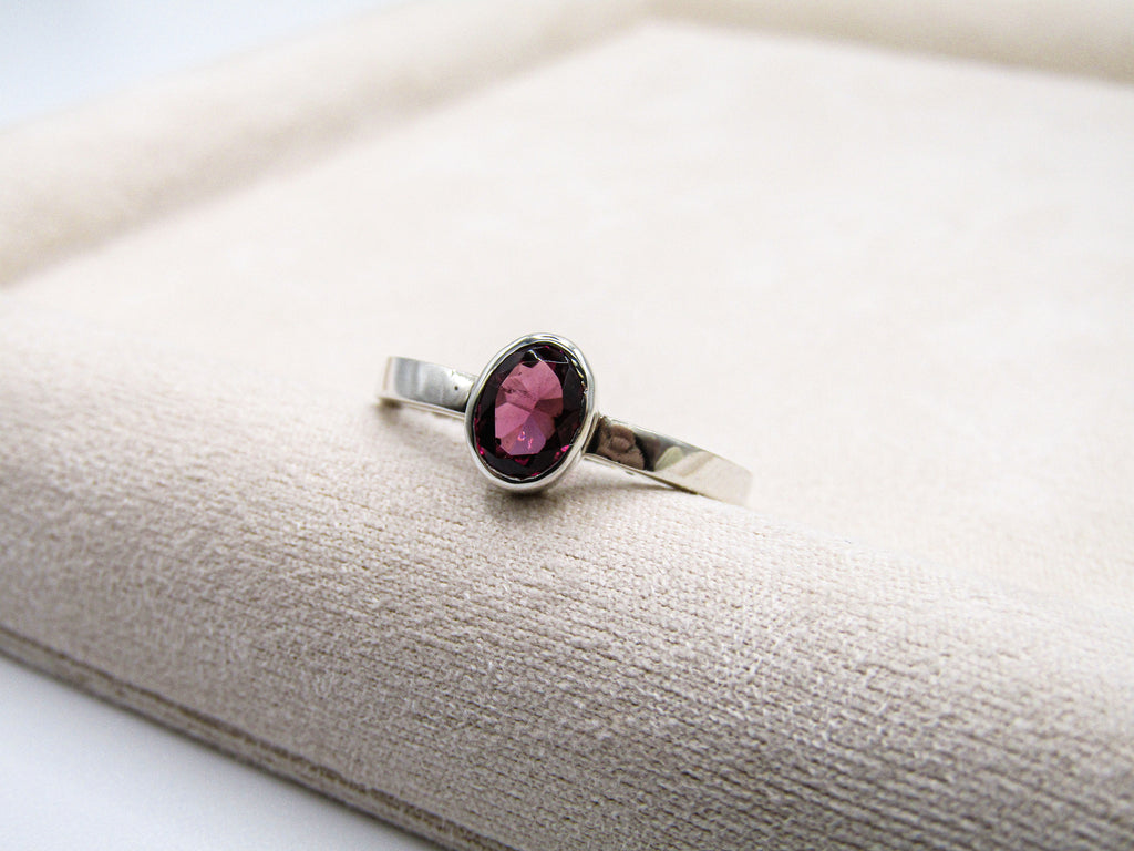 Silver ring with a pink gemstone on a white cushion