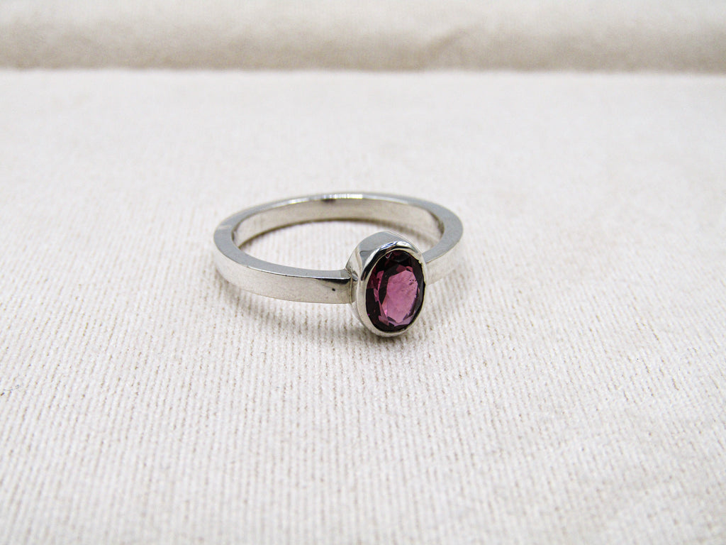 Silver ring with a purple gemstone on a white fabric background