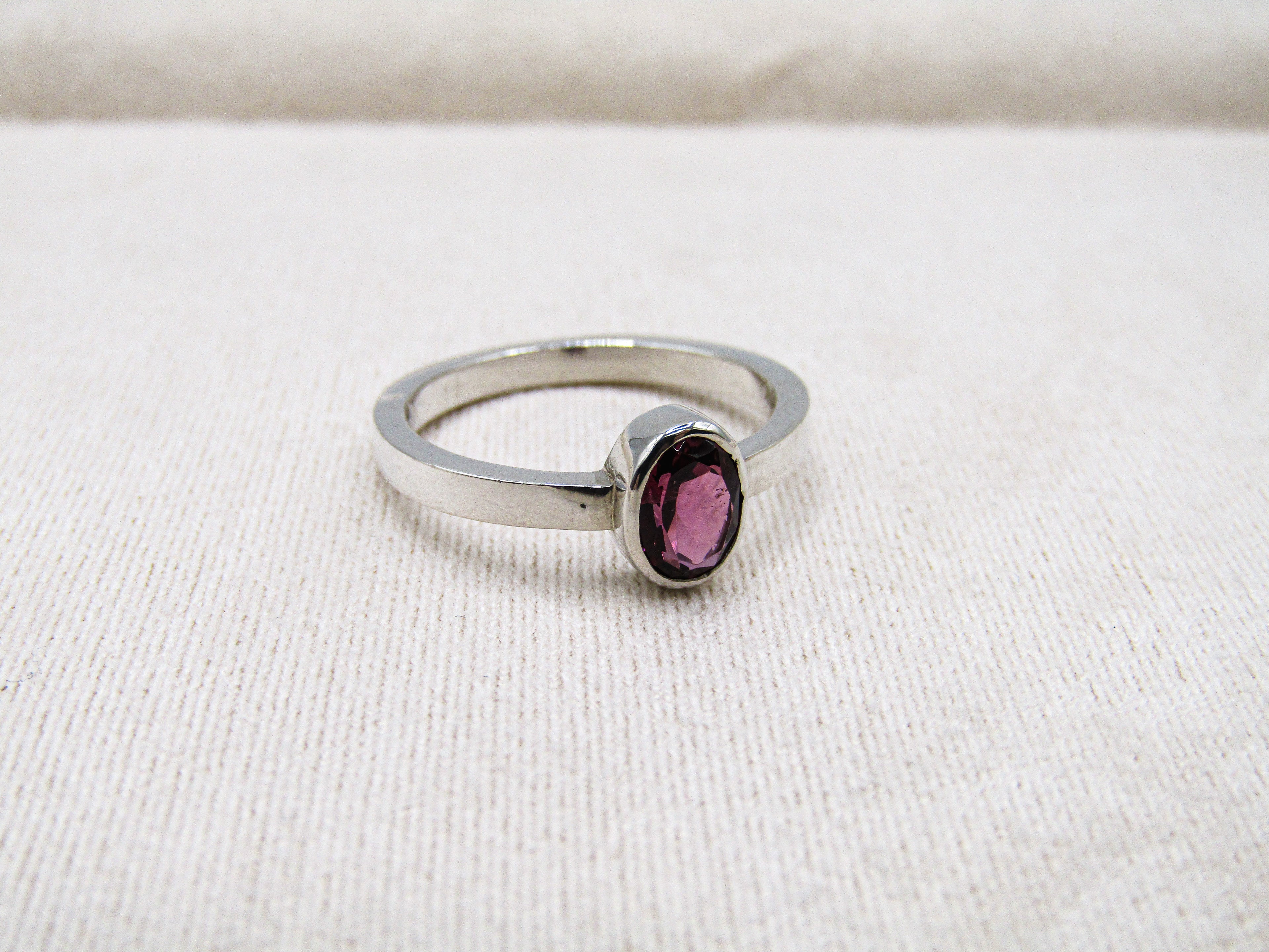 Silver ring with a purple gemstone on a white fabric background