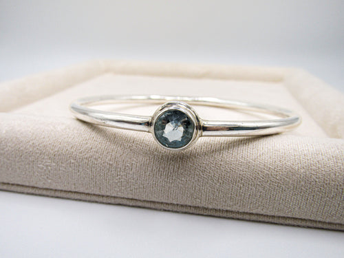 Silver bracelet with a blue gemstone on a beige cushion