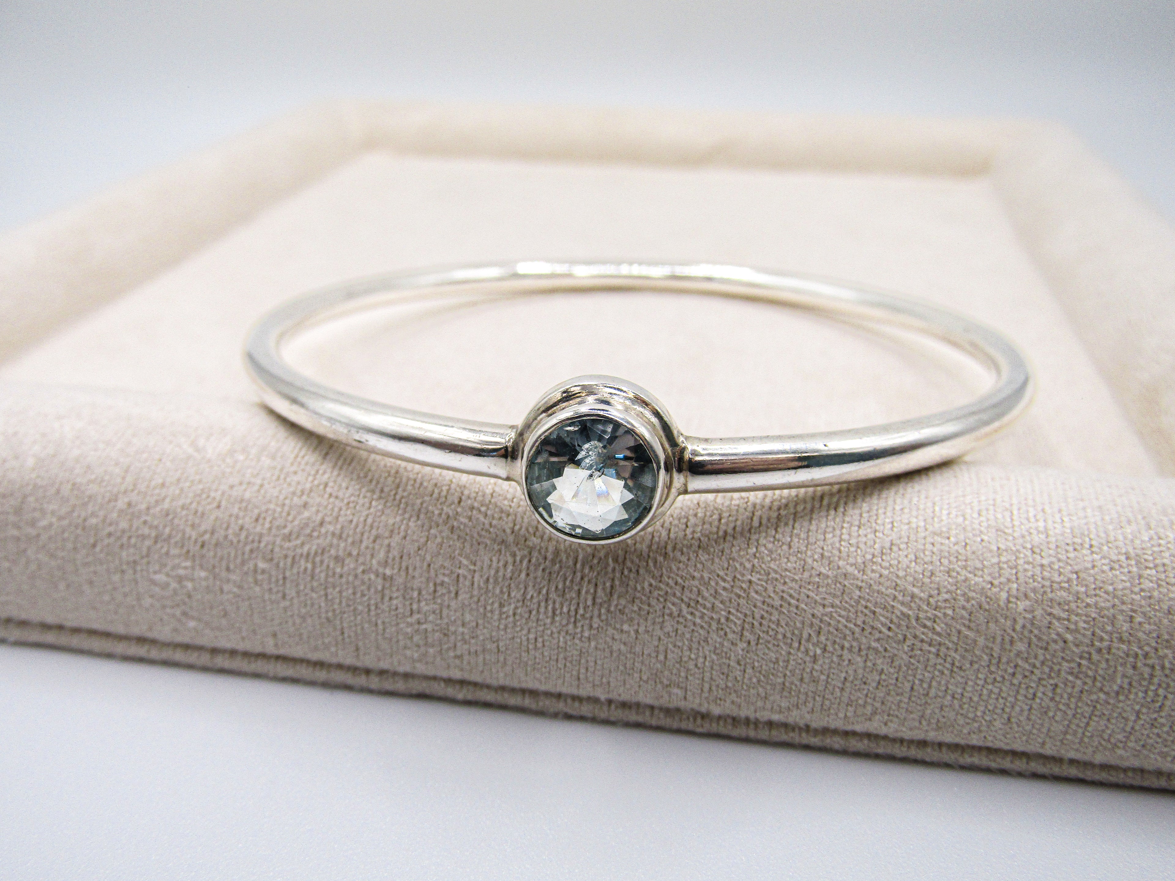 Silver bracelet with a gemstone on a beige cushion