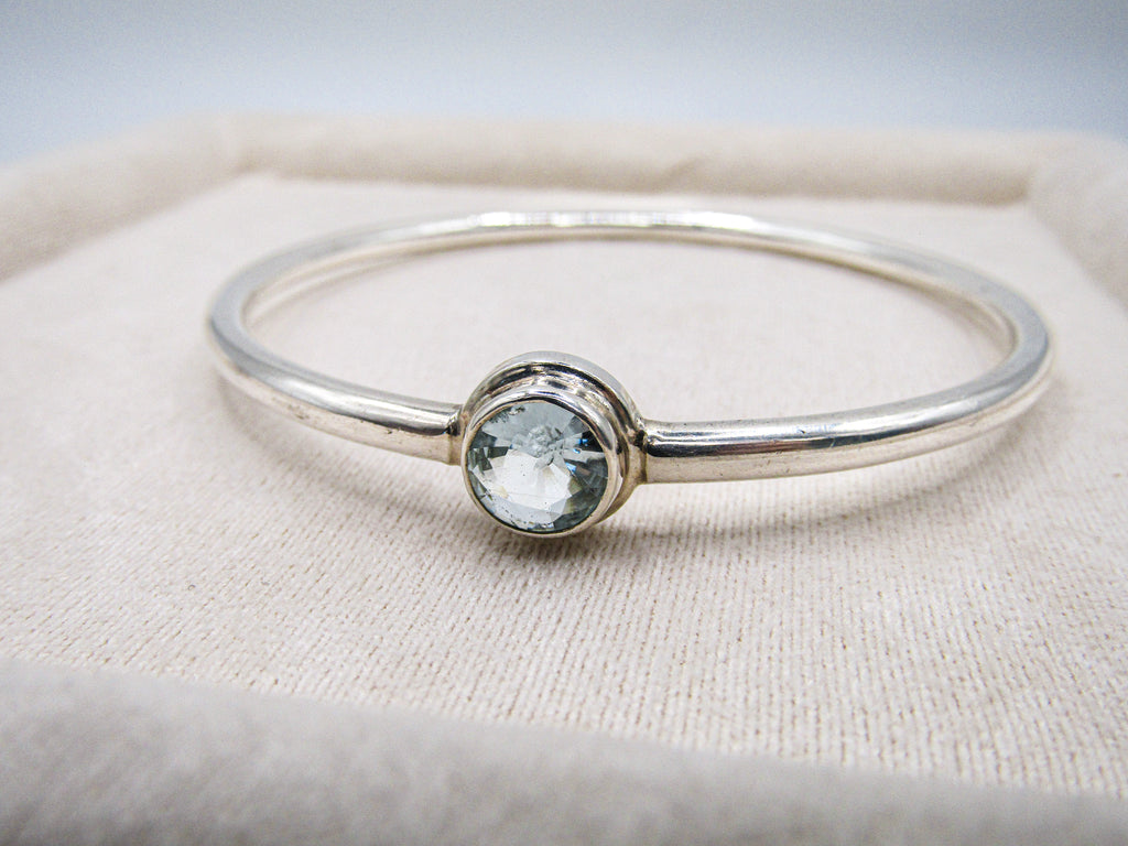 Silver bracelet with a clear gemstone on a beige fabric background