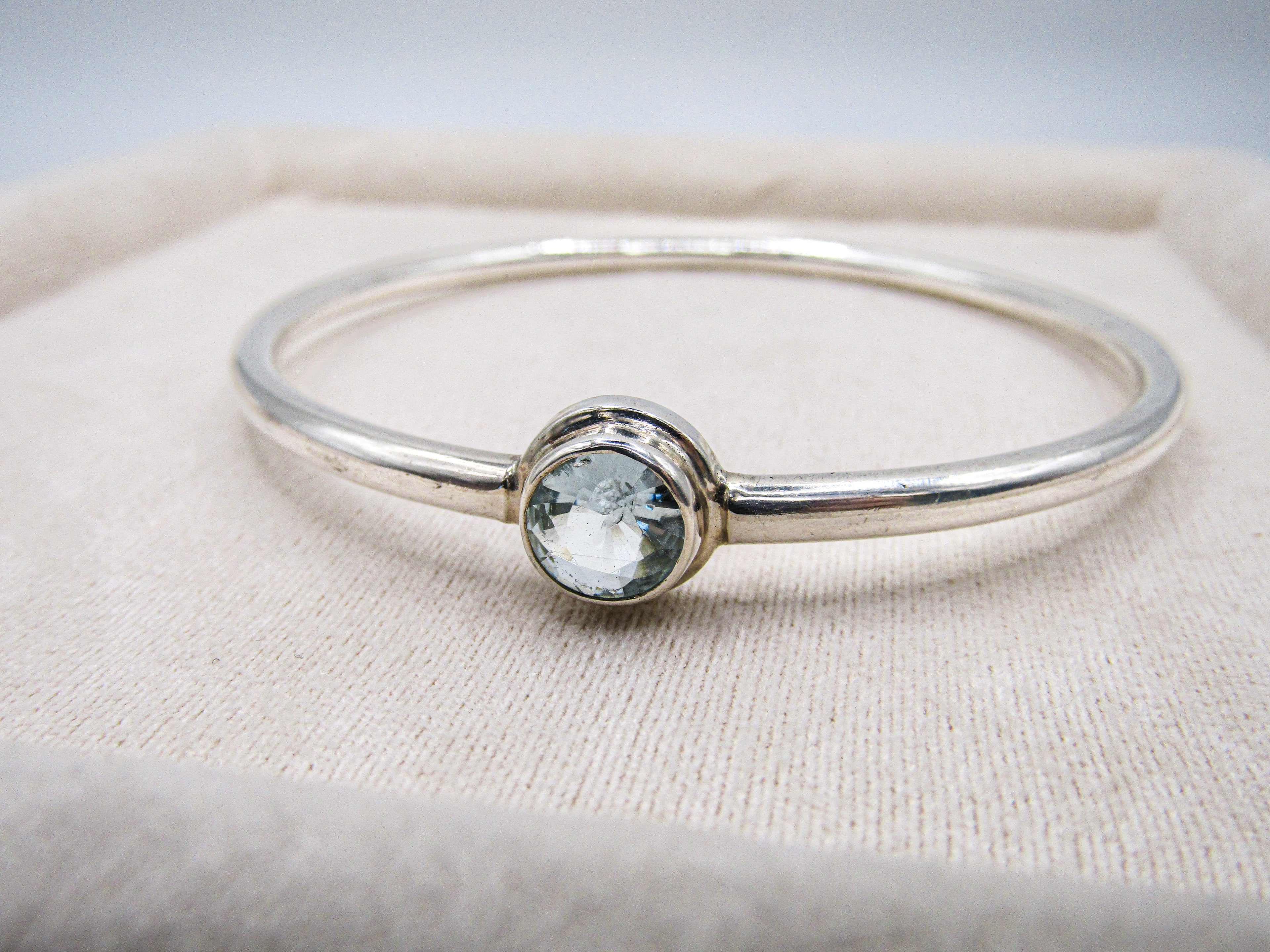 Silver bracelet with a clear gemstone on a beige fabric background