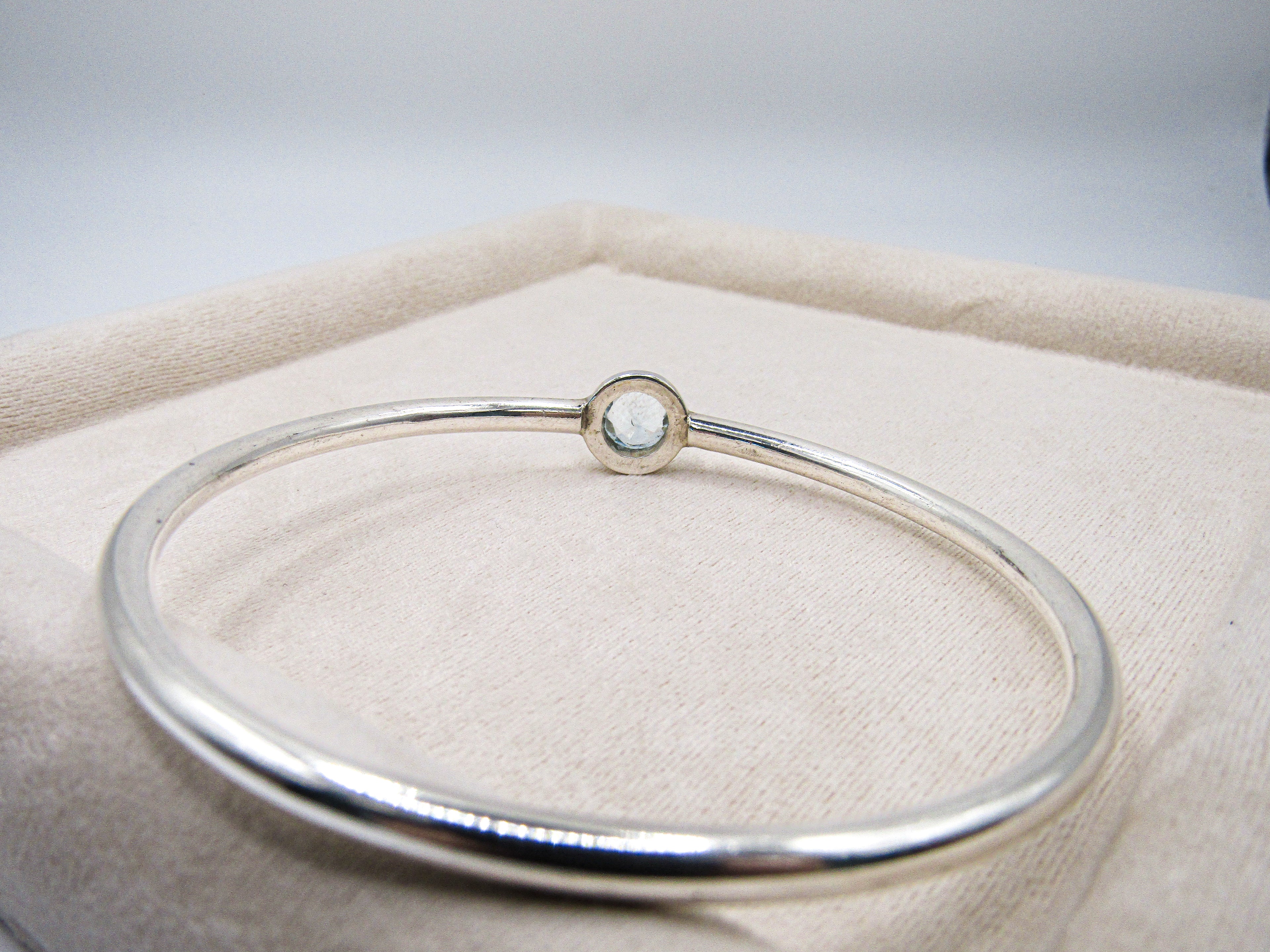 Silver bracelet with a small round gemstone on a beige cushion
