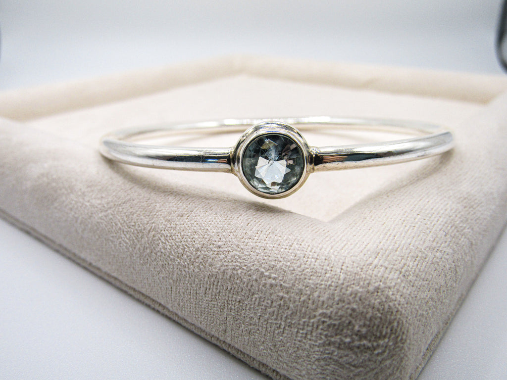 Silver bracelet with a green gemstone on a beige cushion