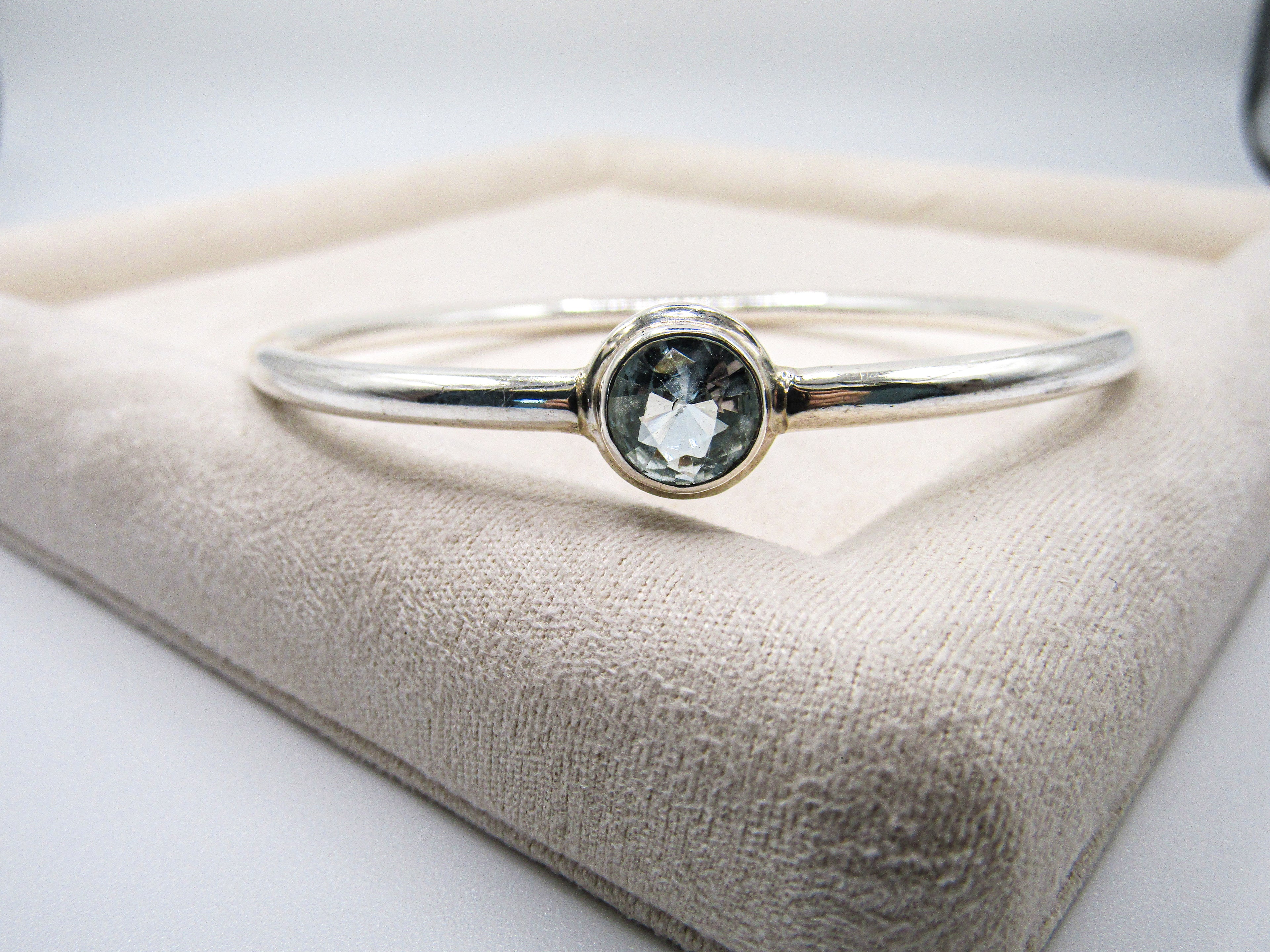 Silver bracelet with a green gemstone on a beige cushion