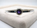 Silver bracelet with a purple gemstone on a textured surface