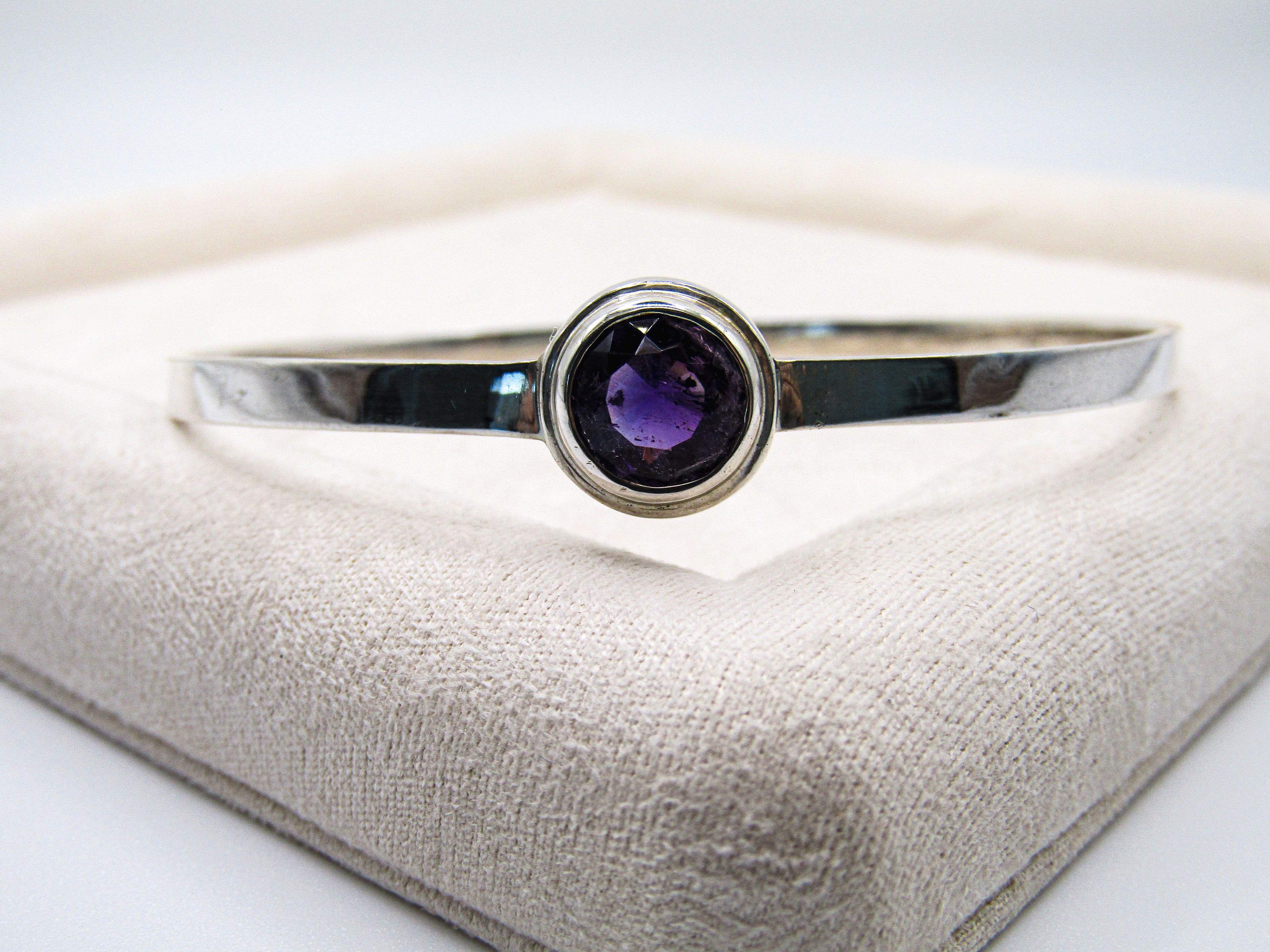 Silver bracelet with a purple gemstone on a textured surface