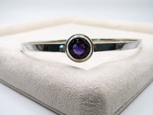 Silver bracelet with a purple gemstone on a textured surface